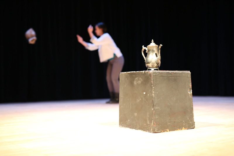 Silver pitcher on a black box and a girl standing in the background