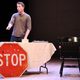 Man standing behind a table, pointing at a stop sign that is leaning up against the table