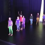 Dancers wearing bright colors standing, looking towards the front of the stage.