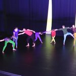 Dancers wearing bright colors holding onto each other.