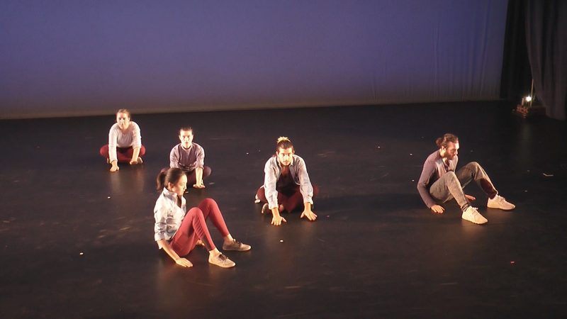 Dancers sitting on the floor with their hands on the ground.