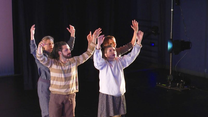 Four dancers looking up with arms raised.