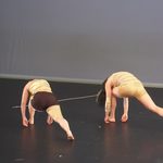 Two dancers wearing gold lunging towards the back of the stage.