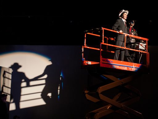 Two actors standing in a raised electric lift with their shadow displayed behind them.