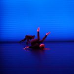 Two dancers onstage in blue light. One is on her back with legs in the air, one crawls upstage.