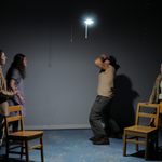 4 people stand on opposite sides of a light bulb. The man in back on the right covers his face.