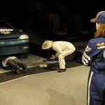 A race car driver in blue watching people fix a car