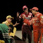 Race car drivers in different colored uniforms shaking hands