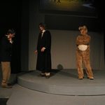 Two men in suits and a person in a bear costume standing on stage