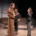 A woman in a black leather jacket looking at a man in a brown cloak