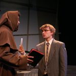 A man in a suit holding a piece of paper at a man in a brown cloak