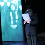 An actor reading from a piece of paper and a projection of an old photo displayed behind