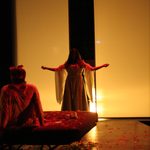 A woman in a dress standing in front of the light next to a bed with rose petals