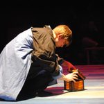 A man kneeling down to open a small wooden box