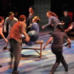 Actors running in a circle around a man seated in the center