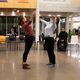 2 dancers perform in Weitz Commons. The dancers stand facing each other leaning back slightly, with arms outstretched.