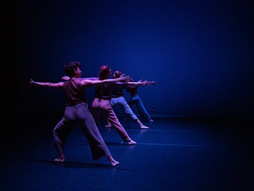 Four dancers are lined up downstage to upstage, with their hands and legs extended, bathed in blue light.