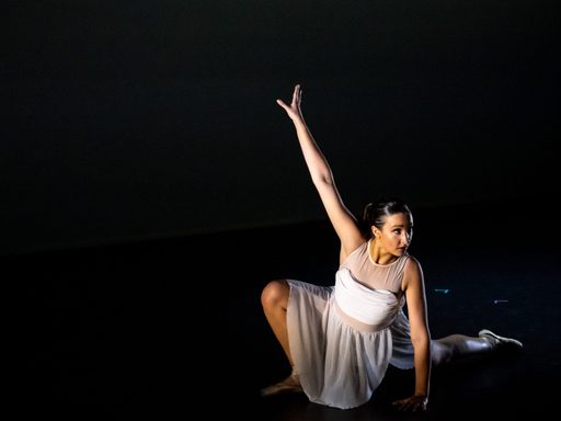 a Dancer in a white outfit crouched down on the floor with her arm extended up