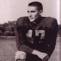 Marck kneels in full football uniform with his elbow resting on his knee