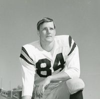 Sundem, wearing #84, kneels on the field, hand resting on his helmet