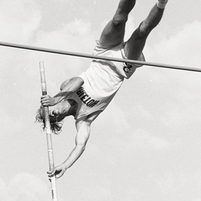 Brown pole vaulting about to leave the pole, legs over the bar