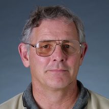 Lunder, weraing glasses and a tan Carleton polo, looking at the camera