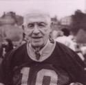Brown as an older man, wearing number 18, poses holding a football under his arm