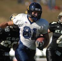 Frank, wearing #81, runs with a football tucked under his left arm, pursued by St. Olaf defense.