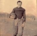 Street stands, helmet tucked under his arm, in an old fashioned football uniform
