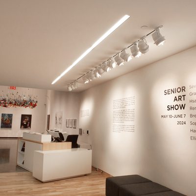 he foyer of the Perlman Teaching Museum. The front desk stands in front of a backless, armless bench, and the words “Senior Art Show: May 10-June 7, 2024” with the student artists’ names are printed on the wall to the desk’s right.