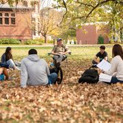 students seated in a circle outdoors among leaves for a class