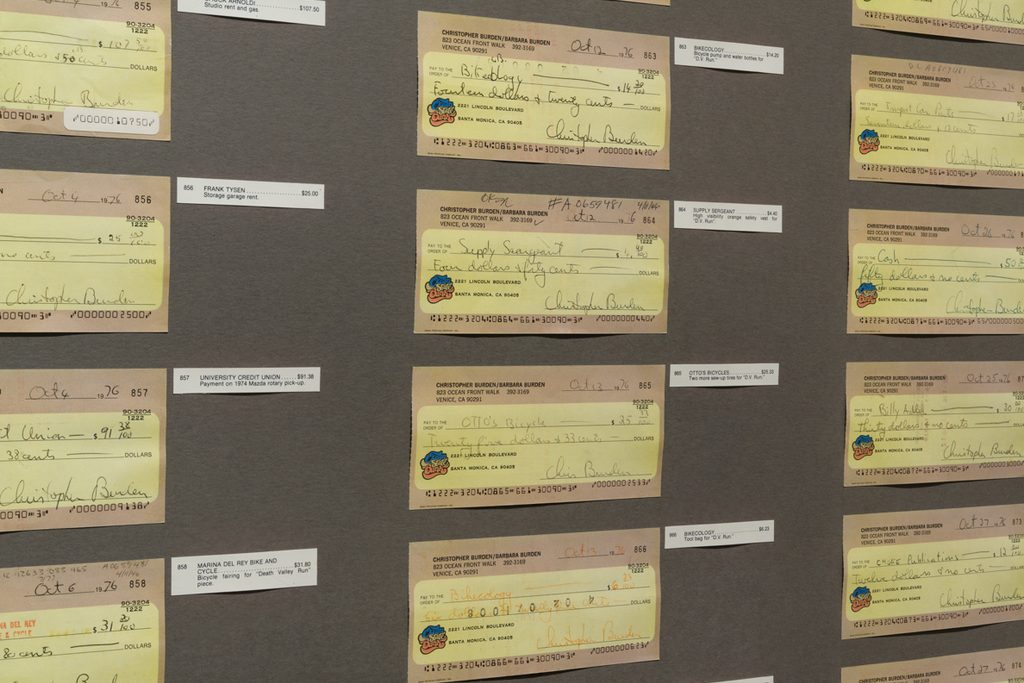 Three symmetrical rows of yellow and brown paper checks, with small white labels, are mounted to a dark gray paper material.