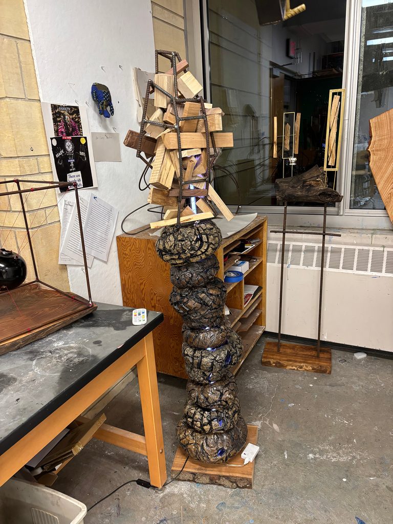 Sculpture in a studio: artwork is crafted from scrap wood, stoneware, black stain, rebar, and more.