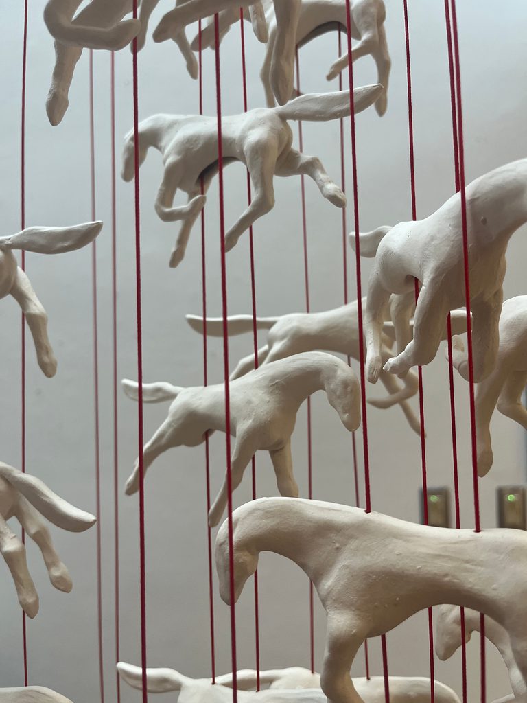 Sculpture of porcelain horses suspended from red cord