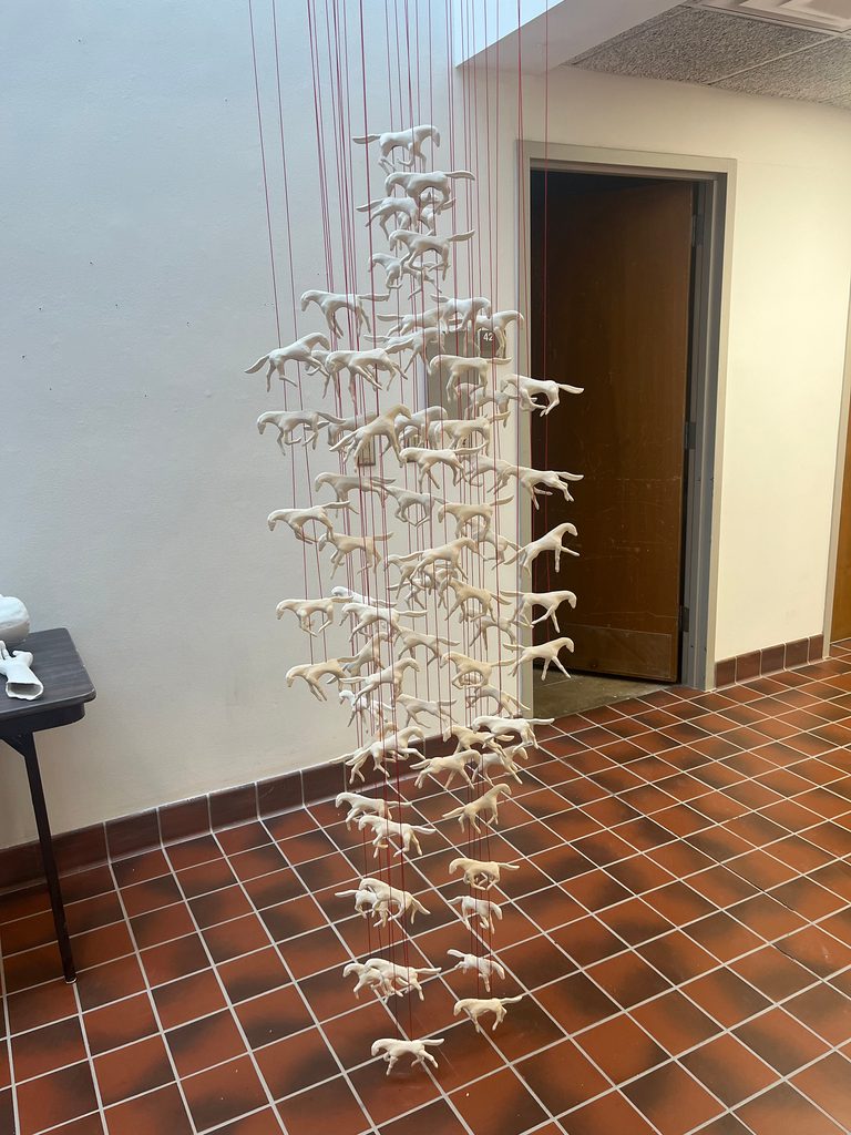 Sculpture of porcelain horses suspended from red cord