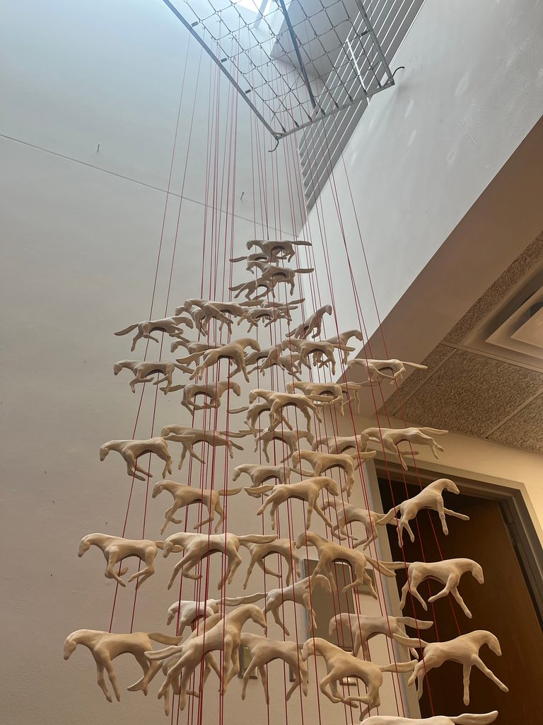 Sculpture of porcelain horses suspended from red cord