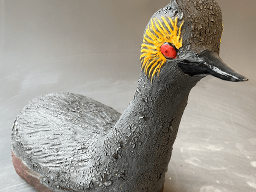 Ceramic sculpture of an eared grebe, a small gray water bird with a bright red eye surrounded by yellow feathers