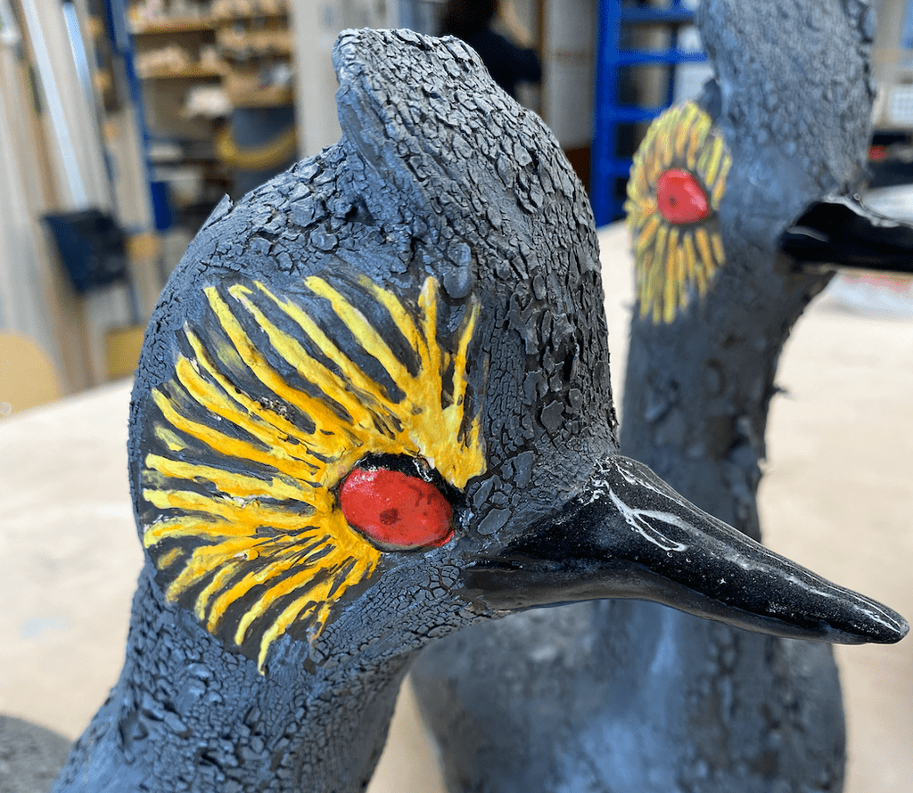 Ceramic sculpture of an eared grebe, a small gray water bird with a bright red eye surrounded by yellow feathers