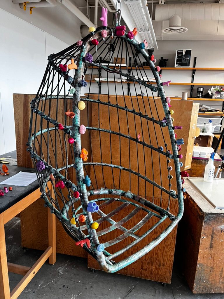 Abstract sculpture made from a metal basket with colorful ceramic objects all suspended from above