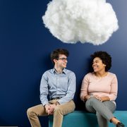 Two smiling students sit on a couch beneath a cotton cloud