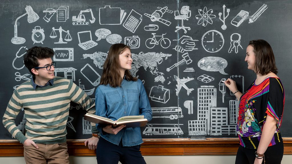 Three students stand in front of an elaborately-illustrated chalkboard