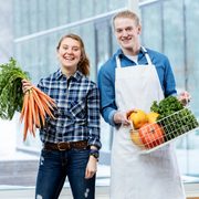 Two students smile and pose with an assortment of fresh vegetables