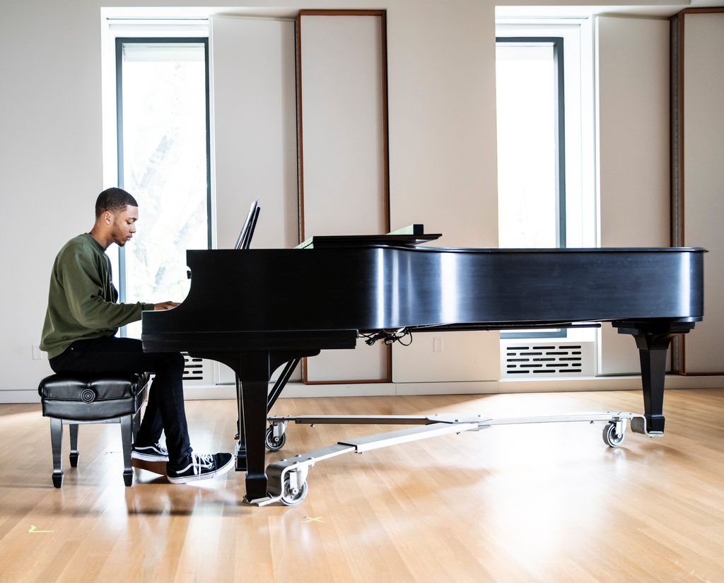 a student plays a grand piano in a light-filled room