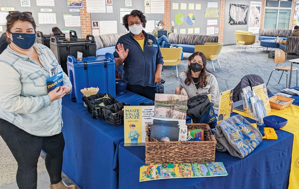 Alumni Annual Fund staff wave from the Maize and Blue Daize trivia prize table in Anderson Hall.