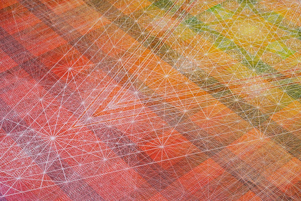 A close up view of a colorful geometric artwork with intersecting white lines forming starburst patterns over layered colors of red, orange, yellow.