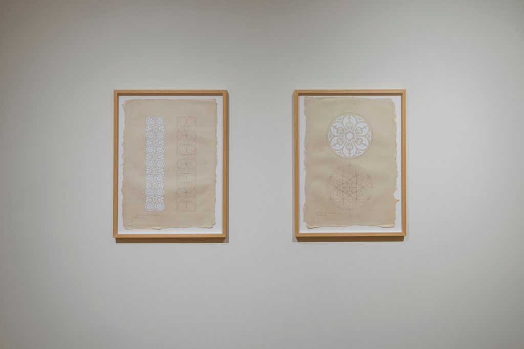 Two framed works of geometric patterned sketches are hung in a gallery with white walls.