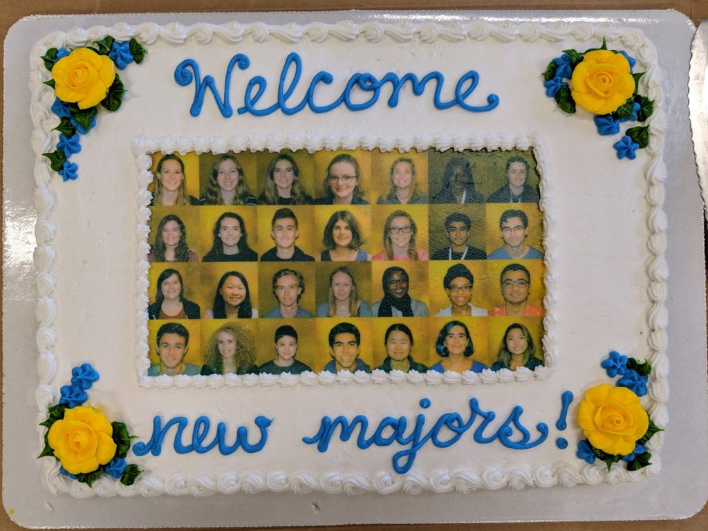 A cake that says "welcome new majors" with photos of all the majors and four yellow flowers
