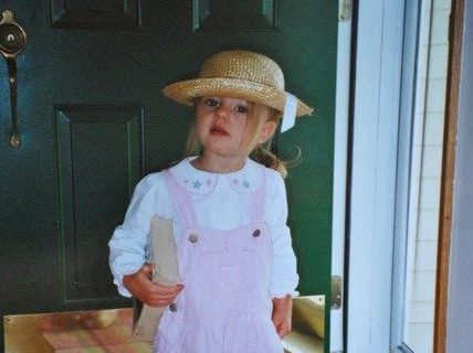 Photo of a young girl holding a book in pink overalls